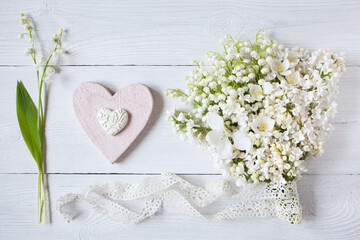 Wall Mural - Bouquet of lilies of the valley, lilac flowers, apple flowers and a heart on a white wooden background. Postcard for wedding, Mother's Day, birthday.