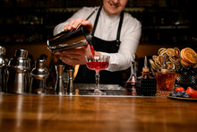 Front View On Bar Counter With A Variety Of Bar Equipment And Goblet In Which Bartender Pours A Cocktail