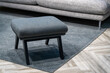 Navy blue stool next to fabric sofa in grey living room interior. Bkue ottoman on a striped carpet
