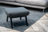 Fototapeta  - Navy blue stool next to fabric sofa in grey living room interior. Bkue ottoman on a striped carpet