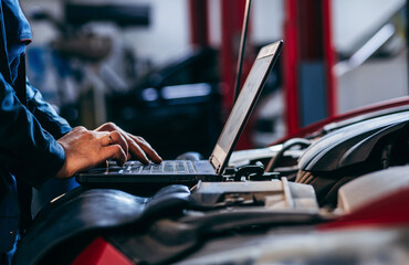 Close up hands of auto electrician using a computer laptop to diagnosing and checking up on car engines parts for fixing and repair