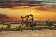 A Rusty Metal Oil Rig Surrounded By Dirt And Green Plants And Grass With Powerful Clouds At Sunset At Bolsa Chica Ecological Reserve In Huntington Beach California USA