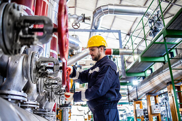 Wall Mural - Refinery worker in protective work wear and yellow hardhat working in petrochemical industry. Factory interior with gas pipeline in background.