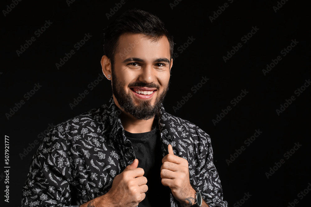 Smiling bearded man adjusting shirt on dark background