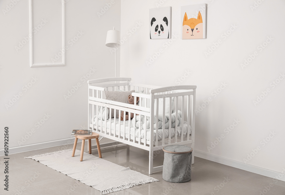 Interior of light nursery with baby crib, lamp and stool