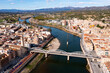 Aerial view of Catalan city of Tortosa on sunny spring day overlooking reconstructed Bridge of State across Ebro river and Monument to Battle of Ebro in middle of water, Spain..