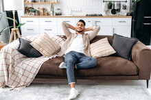 Calm Happy Indian Or Arabian Guy With Eyes Closed, Put Hands Behind Head, Sitting In A Modern Living Room On Comfortable Sofa, Enjoy Calmness And Alone At Home In Weekend, Dreaming, Smiling