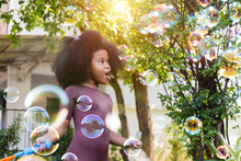 An African American Little Girl In Garden Home Making Big Soap Bubbles