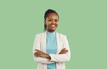 Studio Portrait Of Black Businesswoman With Toothy Smile. Confident Good Looking Young Woman With Afro Braids, In White Jacket And Mint Turtleneck Standing Isolated On Solid Green Colour Background