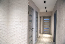 Modern Corridor In An Apartment After Renovation In Gray Tones. Gray Interior Doors And Black LED Lights On The Ceiling. White Brick Wall