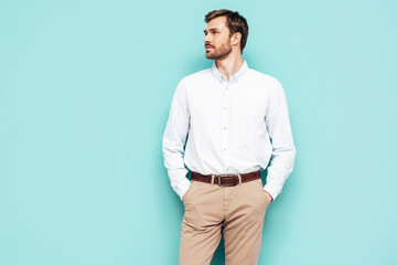 Portrait of handsome confident model. Sexy stylish man dressed in shirt and trousers. Fashion hipster male posing near blue wall in studio