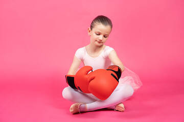 Little classical dancer girl wearing boxing gloves isolated on pink background. Female stereotypes concept.