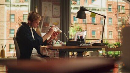 Aufkleber - Talented Male Artist Working on Colorful Wild Brave Design of Sneakers, Uses Laptop Computer in Loft Office Studio. Fashion Designer Customising Pair of Shoes with Shoe Art. New Generation Creatives