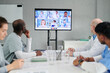 © pressmaster - Group of doctors sitting at table and looking at big screen, they having online meeting with colleagues at office