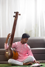 Young Man Reading Musical Note While Practicing Tanpura In Living Room