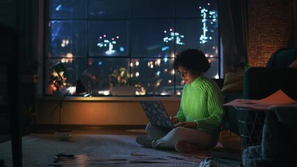 Poster - Black Female Student in Cozy Green Jumper Working at her Laptop During the Evening. Smart Woman Pondering, Smiling, Answering Emails. Girl Study Late at Night