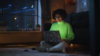 Fototapete - Latina Female Specialist Working on Laptop Computer at Evening while Sitting at the Floor. Freelancer Woman Chatting Over the Internet on Social Networks and Checking her Smartphone