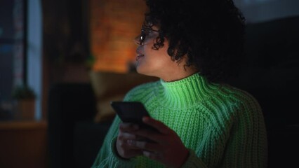 Fototapete - Cinematic Portrait of Black Female with Curly Hair Sitting at the Floor at Home while Using a Smartphone. Diverse Woman Receives Good News and Chatting with Friends. Slow Motion