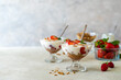Yogurt with strawberry compote and granola, with fresh fruits in dessert cups on grey background. Copy space