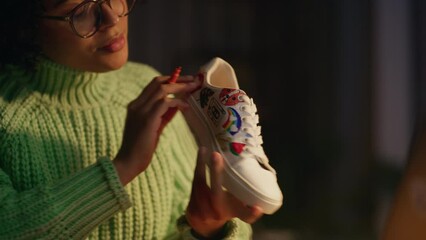 Poster - Close Up Portrait Shot of Black Female Designer Putting Her Individual Drawing on Shoes While Working Late at Evening. Millennial People and Trends in Design Concept