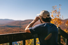 Male Traveler Standing Looking Binoculars On Wooden Footbridge In Mountainous Valley