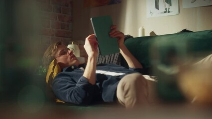 Aufkleber - Young Handsome Man Laying on a Couch in Loft Living Room, Working from Home on Tablet Computer. Creative Male Checking Social Media, Browsing Internet. Millennial People Concept.