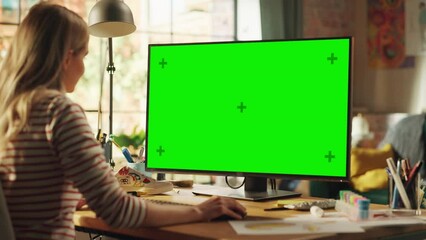 Poster - Over the Shoulder: Creative Young Woman Sitting at Her Desk Using Desktop Computer with Mock-up Green Screen. Female Caucasian Specialist Working on Computer with Chroma Key Display at Home