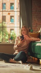 Poster - Caucasian Woman Using Smartphone while Resting at Floor in Cozy Stylish Apartment. Female Blogger Creating Content and Scrolling Over the Internet. Using Social Networks Concept. Vertical Shot