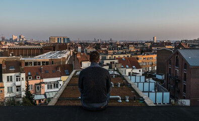 Forty year old man sitting on the roof overlooking the Brussels skyline during sunset