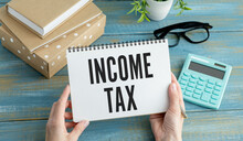 Income Tax Text On Paper Sheet With Magnifying Glass On Chart, Dice, Spectacles, Pen, Laptop And Blue And Yellow Push Pin On Wooden Table - Business, Banking, Finance And Investment Concept