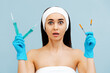 © _KUBE_ - Portrait of a amazement pretty young woman holding four syringes for injection. Light blue background. The concept of plastic surgery and rejuvenation