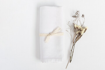 Linen napkin tied with ribbon on white table. Fabric and dried flowers in rustic style for mock up