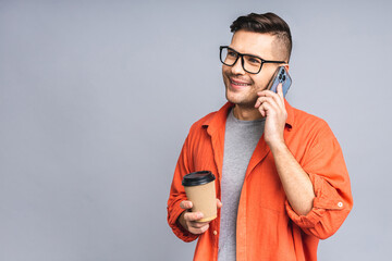 Oh, great news! Smiling young casual man in glasses talking on the mobile phone isolated over white grey background.