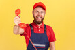 © khosrork - Portrait of positive handyman wearing blue uniform holding out handset, asking call him and order service, looking at camera happy expression. Indoor studio shot isolated on yellow background.