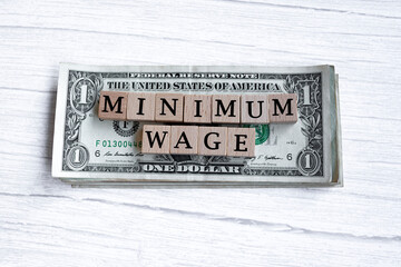 Minimum wage word written on wood block with American Dollar-bills. 