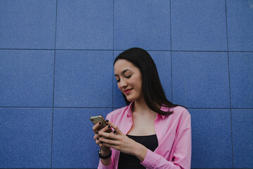 Wall Mural - smiling young woman using mobile phone on wall