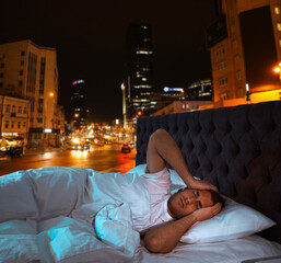 Sticker - Annoyed man in bed and beautiful view of night cityscape on background. Poor sleep because of urban noise