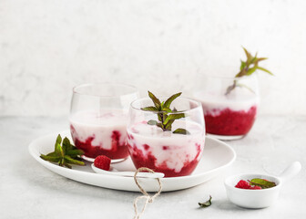 Delicious buttermilk smoothie drink with raspberry sauce decorated with fresh peppermint leaves garnish in glasses. Homemade healthy food concept. Copy space.