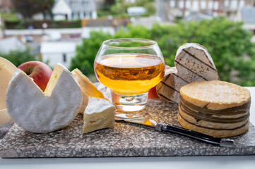 Cow cheeses of Normandy - camembert, livarot, neufchatel, pont l'eveque and glass of apple cider drink with houses of Etretat village on background, Normandy, France