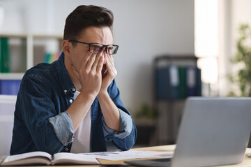 Eyes Strain. Overworked Young Businessman Tired After Working With Laptop In Office