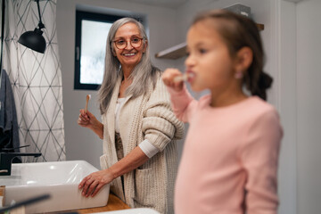 Wall Mural - Senior grandmother making a ponytail to her granddaughter indoors in bathroom in the morning.