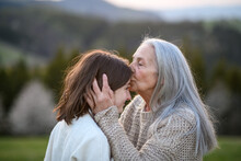 Happy Senior Grandmother Kissing Her Teenage Granddaguhter On Forehead In Nature On Spring Day.