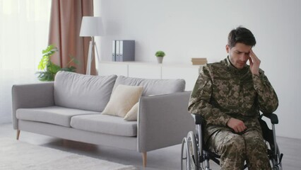 Wall Mural - Military traumas. Young man veteran in camouflage uniform suffering from depression, sitting alone in wheelchair at home