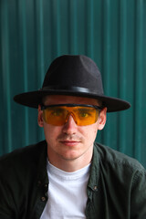 Happy fashion man. Portrait of handsome smiling stylish hipster lambersexual model. Man dressed in yellow sunglasses and black hat. Fashion male on the modern background. Caucasian. Guy. Boy