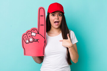 Wall Mural - young adult woman looking shocked and surprised with mouth wide open, pointing to self. number one fan concept