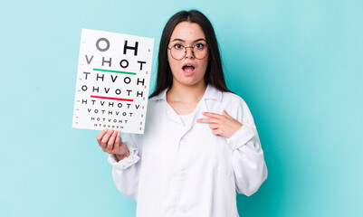 Wall Mural - young adult woman looking shocked and surprised with mouth wide open, pointing to self. optical vision test concept