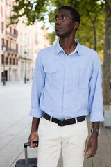 Wall Mural - Portrait of an african american tourist on the street of european city with suitcase