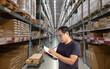 © Itsanan - Warehouse worker writing on book. Distribution warehouse interior with shelve and boxes.