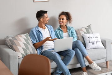 Wall Mural - Young couple with laptop video chatting on sofa at home