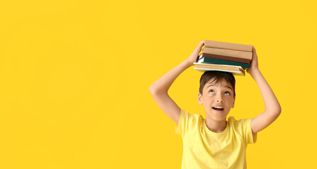 Wall Mural - Little boy holding stack of books on yellow background